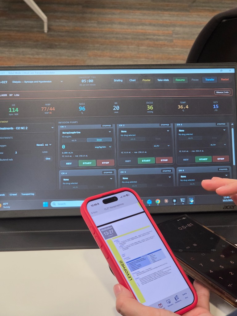 The simulator on a monitor, norepinephrine running on channel 1, with a phone open to the Levophed reference.